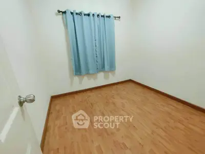 Spacious empty room with wooden flooring and blue curtains, perfect for customization.