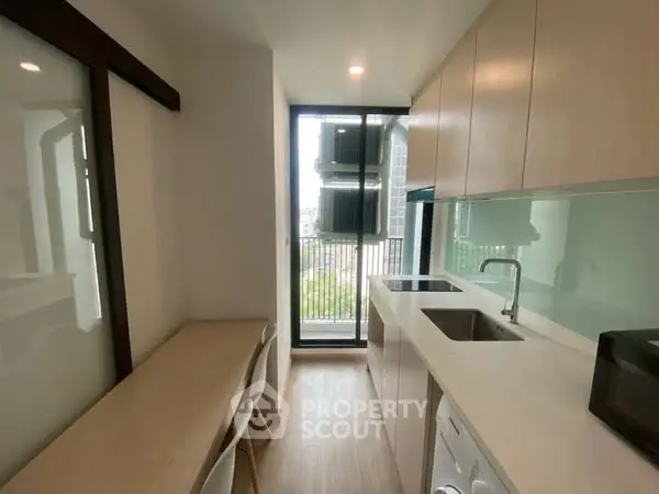 Modern kitchen with sleek cabinetry and balcony view, featuring built-in appliances and natural light.