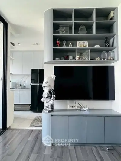 Modern living room with sleek shelving and large TV, adjacent to a stylish kitchen.