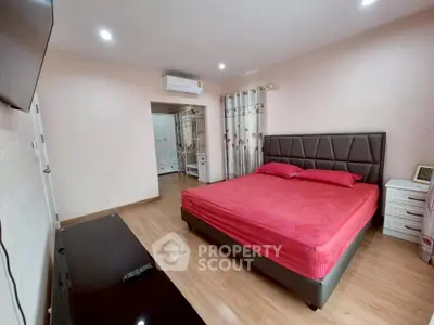 Spacious bedroom with modern decor and red bedding, featuring a sleek air conditioning unit and wooden flooring.