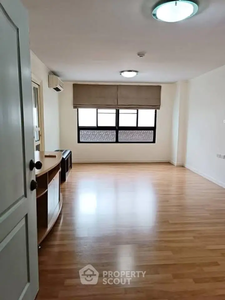 Spacious empty living room with wooden flooring and large window.