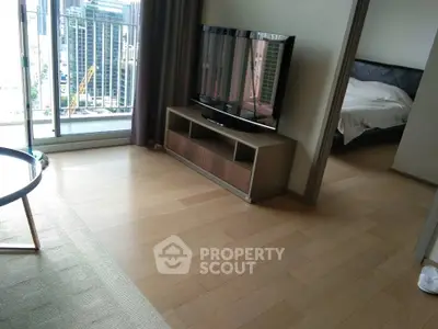 Modern living room with wooden flooring, TV, and balcony view in urban apartment.