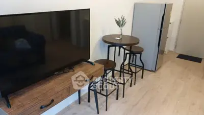 Modern living room with sleek TV, stylish wooden furniture, and compact kitchen area.