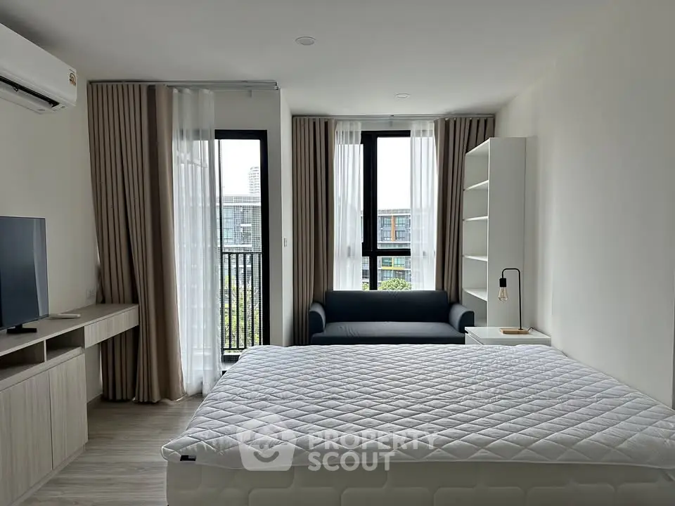 Modern bedroom with large windows, cozy sofa, and stylish decor in a contemporary apartment.