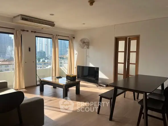 Spacious living room with large windows offering city views, modern furniture, and natural light.