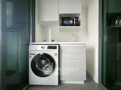 Modern compact kitchen with washing machine and microwave in sleek white cabinetry.