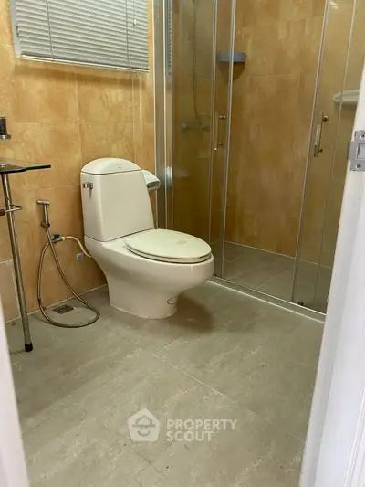 Modern bathroom with glass shower and beige tiles, featuring a sleek toilet and contemporary fixtures.