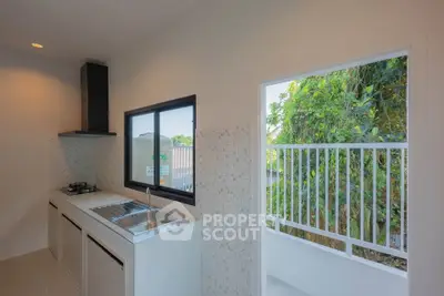 Modern kitchen with open layout and gas stove, featuring a view of lush greenery through the window.