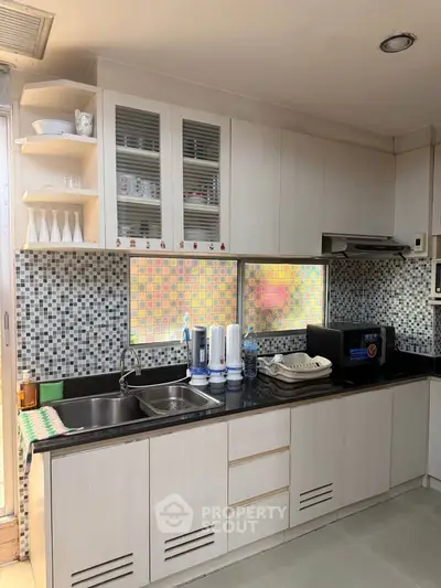 Modern kitchen with sleek cabinetry and mosaic backsplash, featuring a microwave and water filtration system.
