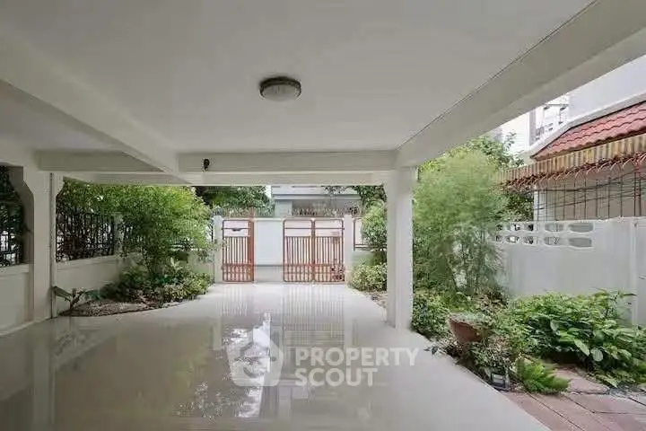 Spacious covered parking area with lush greenery and secure gate access.