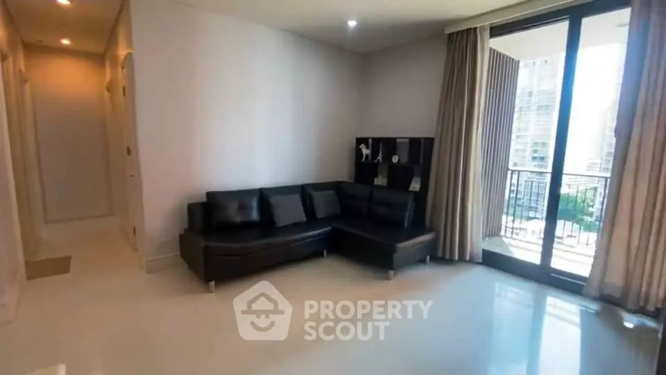 Spacious living room with modern black sofa and balcony view in a high-rise apartment.