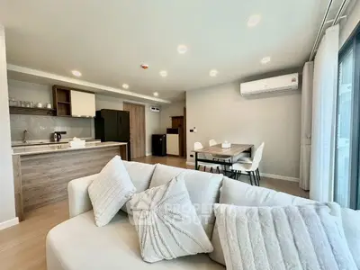 Modern open-plan living room with stylish kitchen and dining area, featuring cozy sofa and natural light.