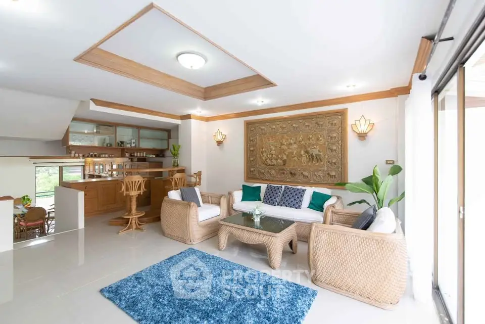 Spacious living room with elegant decor and natural light, featuring wicker furniture and a vibrant blue rug.