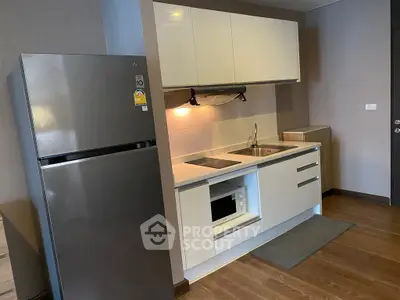 Modern kitchen with sleek cabinetry and stainless steel fridge in a cozy apartment.