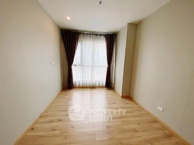 Spacious empty room with wooden flooring and large window, perfect for customization.