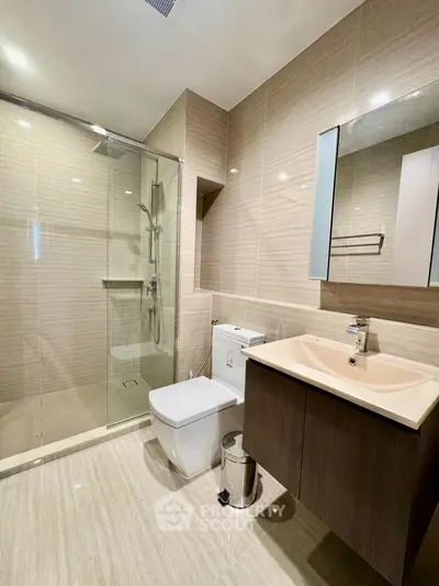 Modern bathroom with glass shower, sleek vanity, and neutral tiles.
