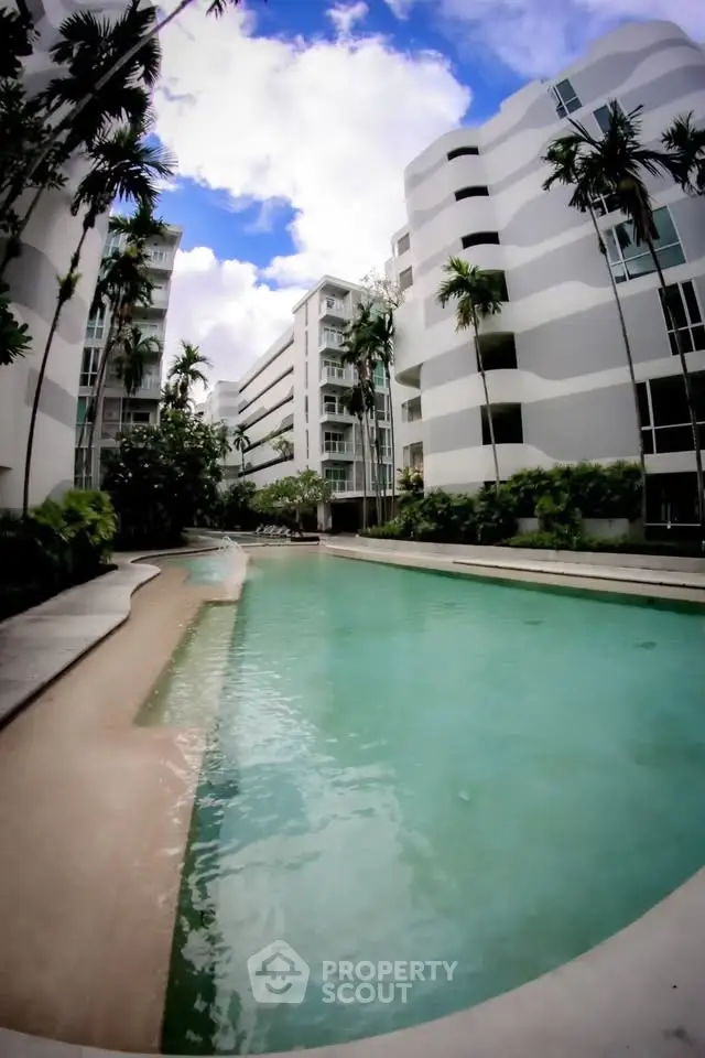 Luxurious apartment complex with stunning pool and modern architecture under a vibrant blue sky.