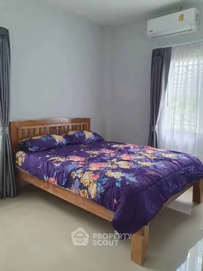 Cozy bedroom with wooden bed frame and floral bedding, featuring natural light and air conditioning.
