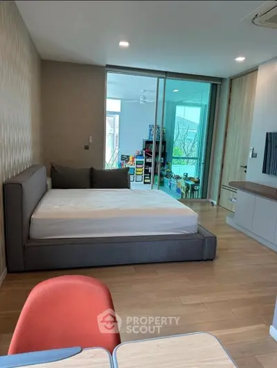 Modern bedroom with sliding glass doors and a view of a playroom, featuring sleek furniture and wooden flooring.