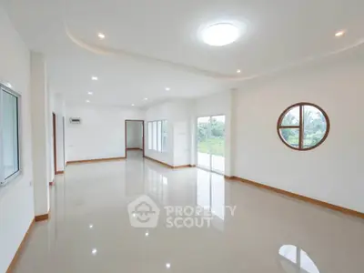 Spacious modern living room with large windows and circular window offering natural light and garden view.