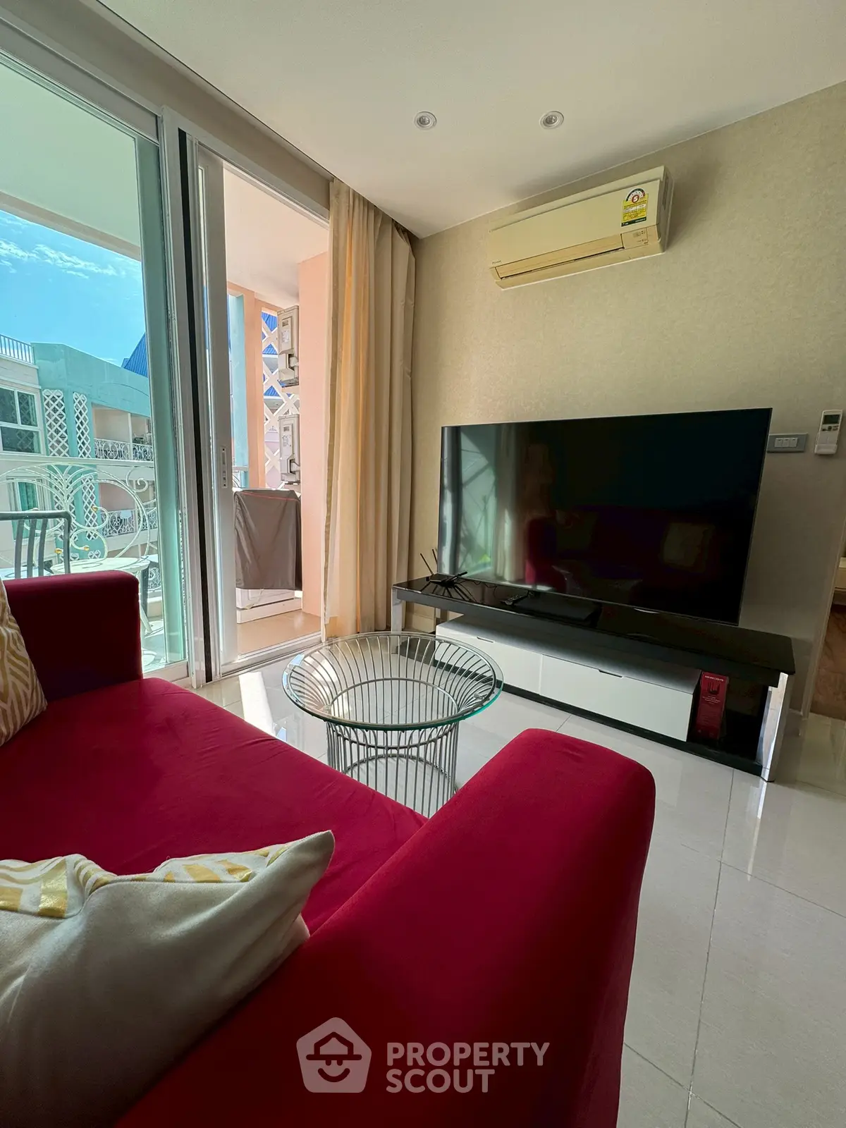 Modern living room with red sofa and large TV, opening to a sunny balcony.