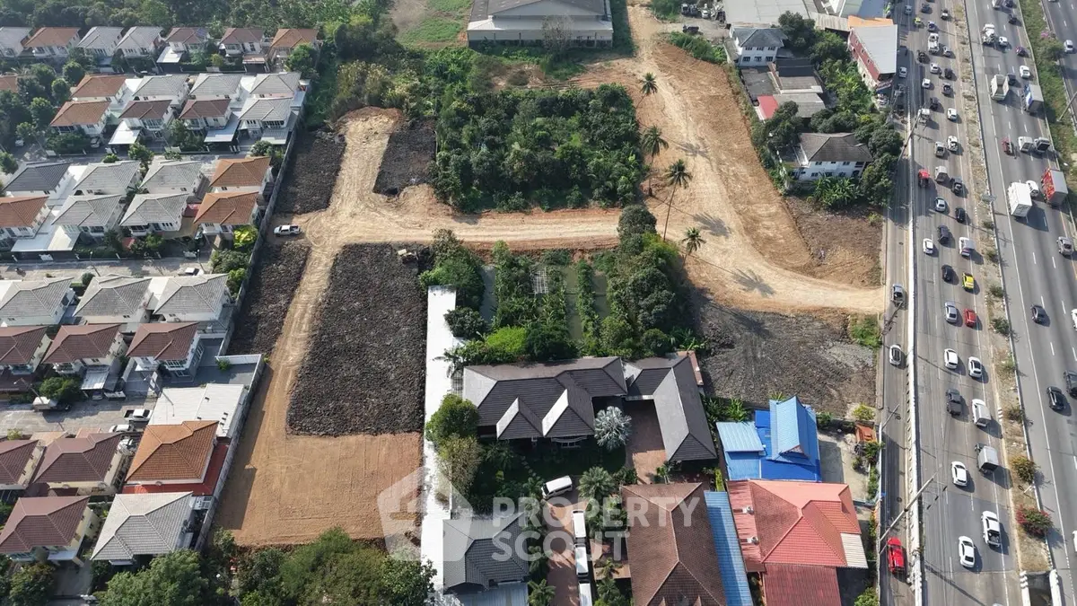 Aerial view of residential area with houses and adjacent undeveloped land near a busy highway.