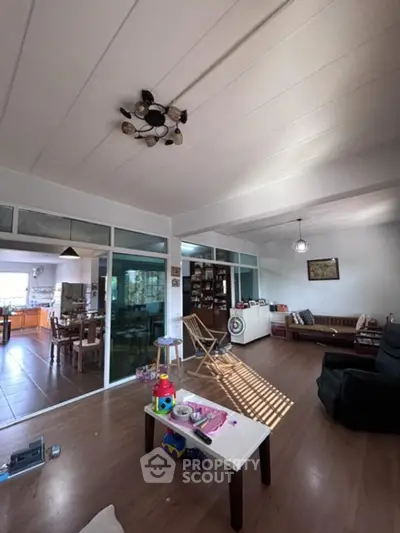 Spacious living room with high ceilings, sleek hardwood floors, and abundant natural light from floor-to-ceiling windows, seamlessly connecting to an open kitchen area.