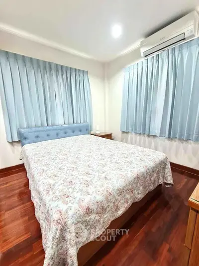 Cozy bedroom with wooden flooring and blue curtains, featuring a comfortable bed and air conditioning.