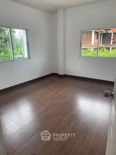 Spacious empty room with wooden flooring and large windows offering natural light.