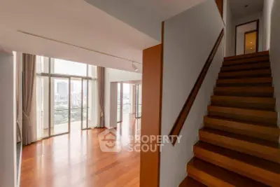 Spacious modern living room with wooden floors and large windows offering city views.
