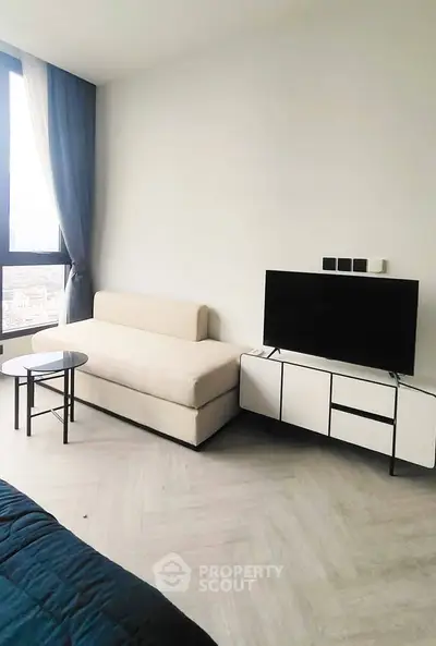 Modern living room with sleek furniture and large window offering city views.