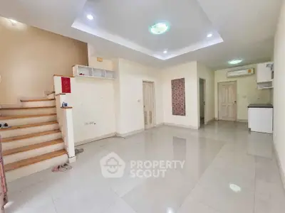Spacious empty living room with modern lighting and staircase, ideal for customization.