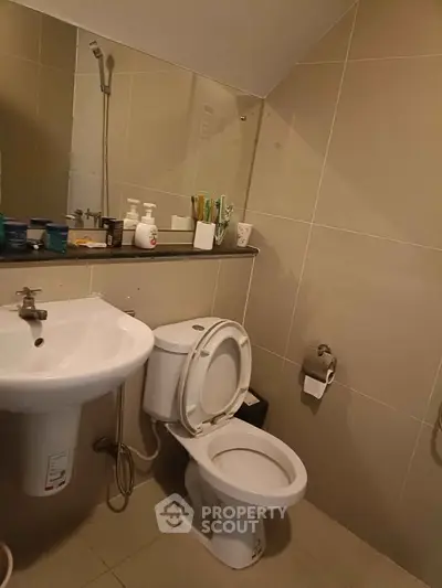 Modern bathroom with sleek fixtures and neutral tiles, featuring a toilet, sink, and mirror.