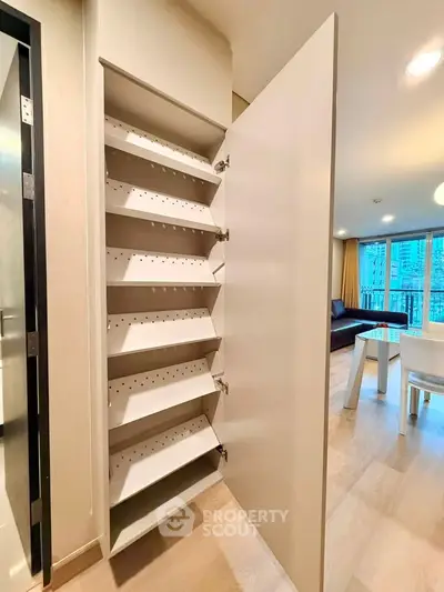 Modern apartment interior with open storage cabinet and view of living room and balcony.
