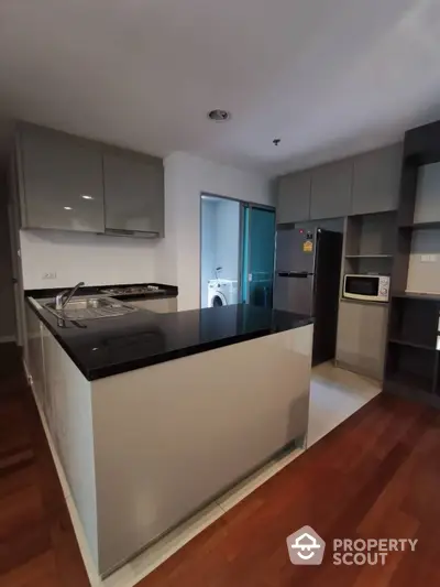 Modern kitchen with sleek cabinetry and built-in appliances, featuring a central island, hardwood flooring, and a view into a well-lit living space.