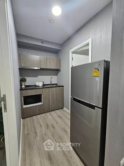 Modern compact kitchen with sleek cabinetry and stainless steel fridge in a stylish apartment.
