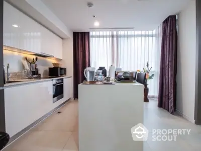 Modern kitchen with sleek white cabinets and island, featuring natural light and elegant decor.