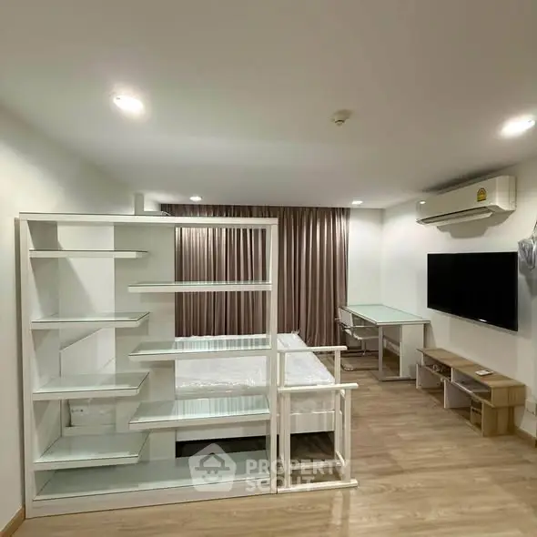 Modern studio apartment with sleek furniture and wooden flooring, featuring a wall-mounted TV and air conditioning.
