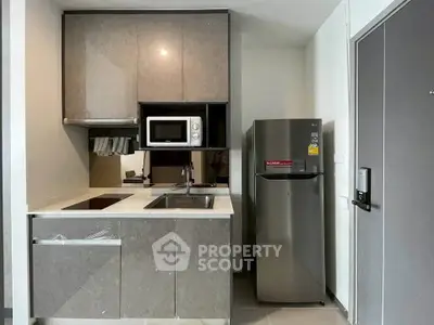 Modern compact kitchen with sleek cabinetry, stainless steel fridge, and built-in microwave in urban apartment.