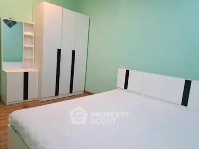 Spacious bedroom with modern white furniture and mint green walls.