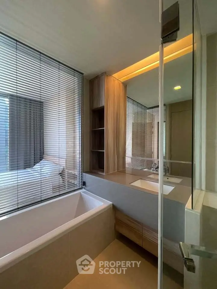 Modern bathroom with sleek design and large window overlooking bedroom, featuring a bathtub and stylish vanity.