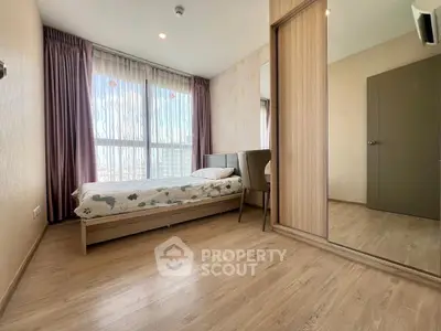 Spacious bedroom with large window and wooden flooring, perfect for relaxation.
