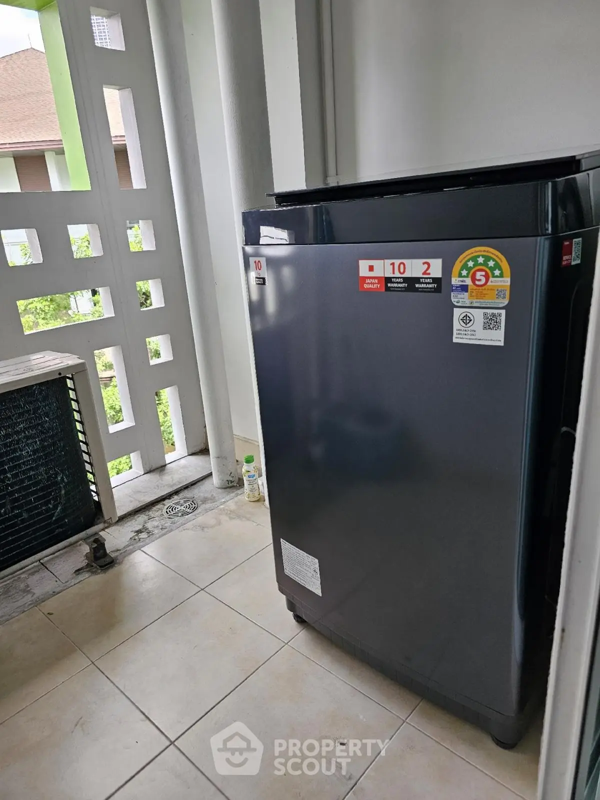 Modern washing machine on tiled balcony with partial view of greenery.