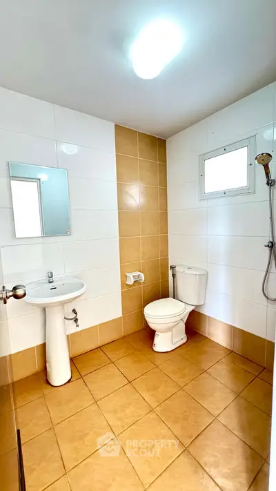 Modern bathroom with tiled walls, pedestal sink, and showerhead in a bright setting.