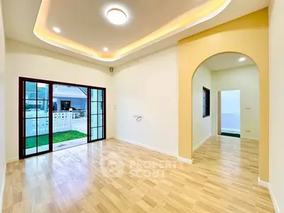 Spacious living room with elegant lighting and wooden flooring, featuring large sliding doors opening to a garden view.