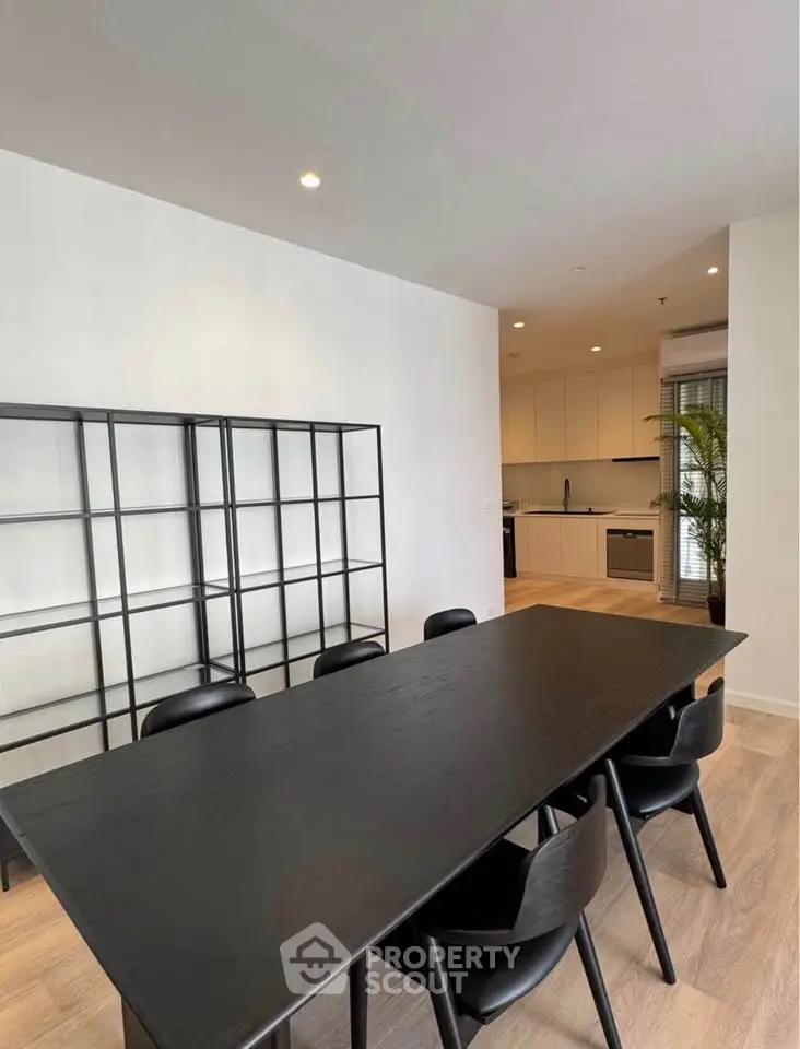 Modern dining area with sleek black table and chairs, adjacent to a contemporary kitchen with minimalist design.