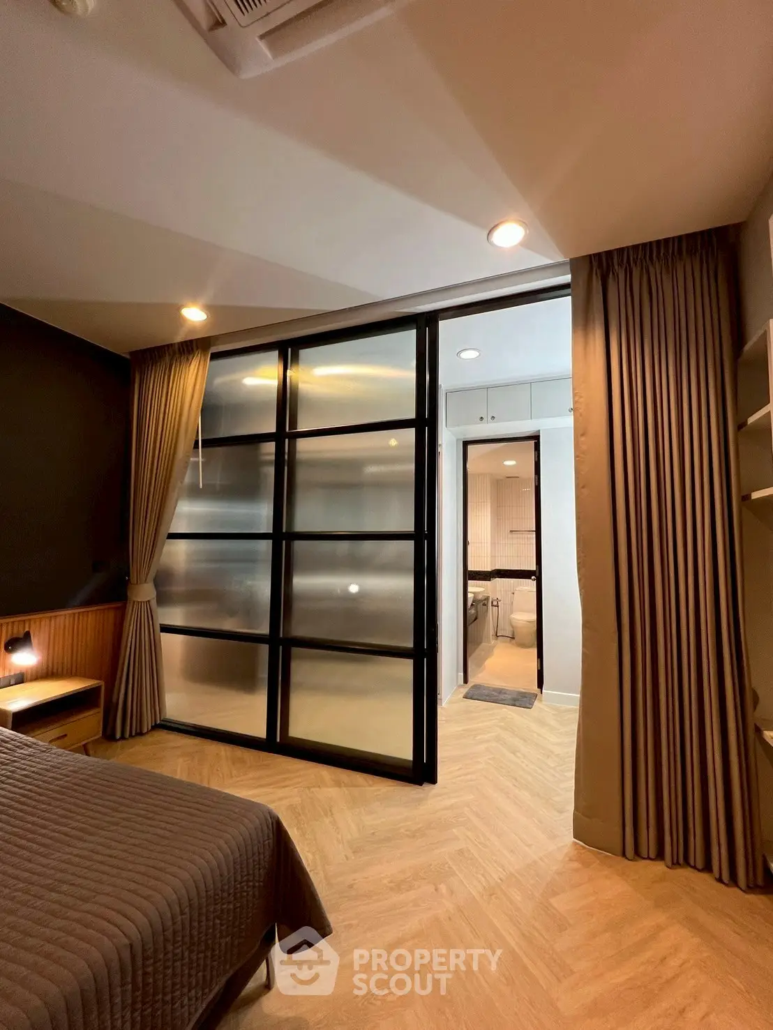 Modern bedroom with sliding glass door leading to a stylish bathroom, featuring elegant lighting and wooden flooring.
