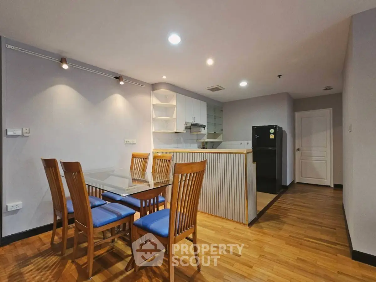 Spacious dining area with wooden flooring and modern kitchen in open layout apartment.