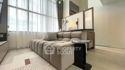 Modern living room with plush sofa and large windows, featuring elegant decor and natural light.