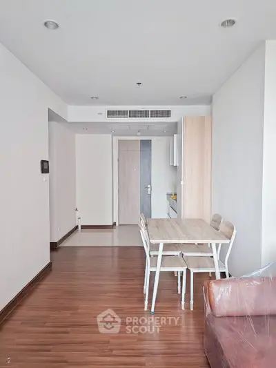 Modern apartment interior with wooden flooring and dining area, showcasing minimalist design and natural light.